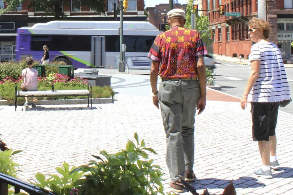 Two people walking away from camera through pedestrian plaza in street in Richmond, Virginia with purple and white city bus moving in background.
